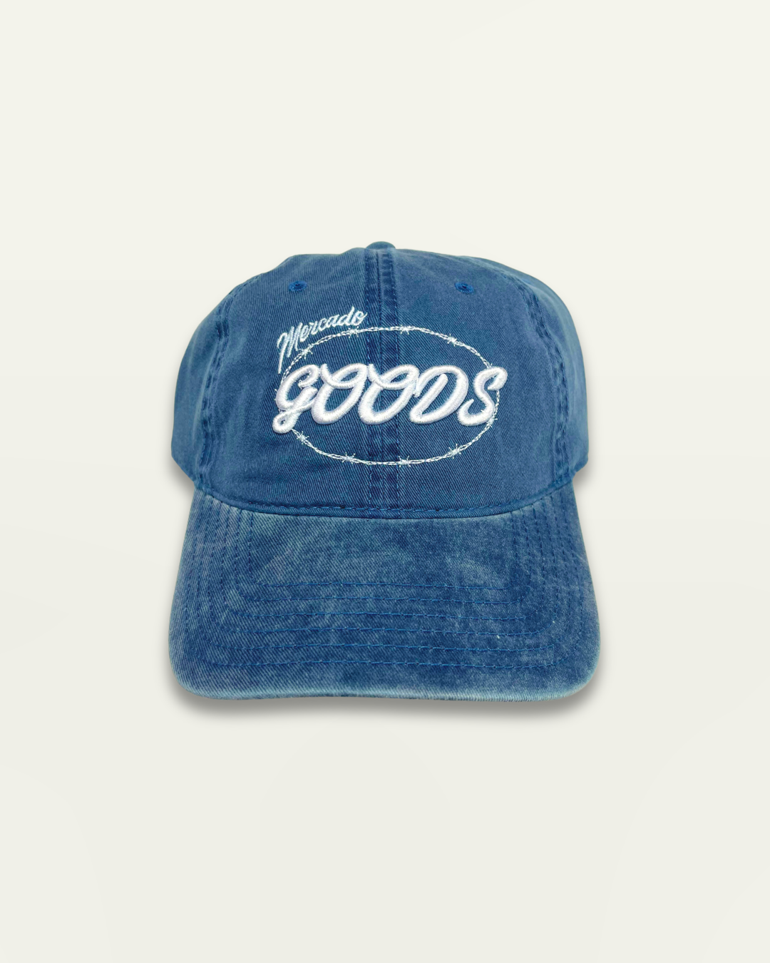 A washed blue denim baseball cap with 'Mercante Goods' embroidered in white script on the front, set against a solid off-white background.